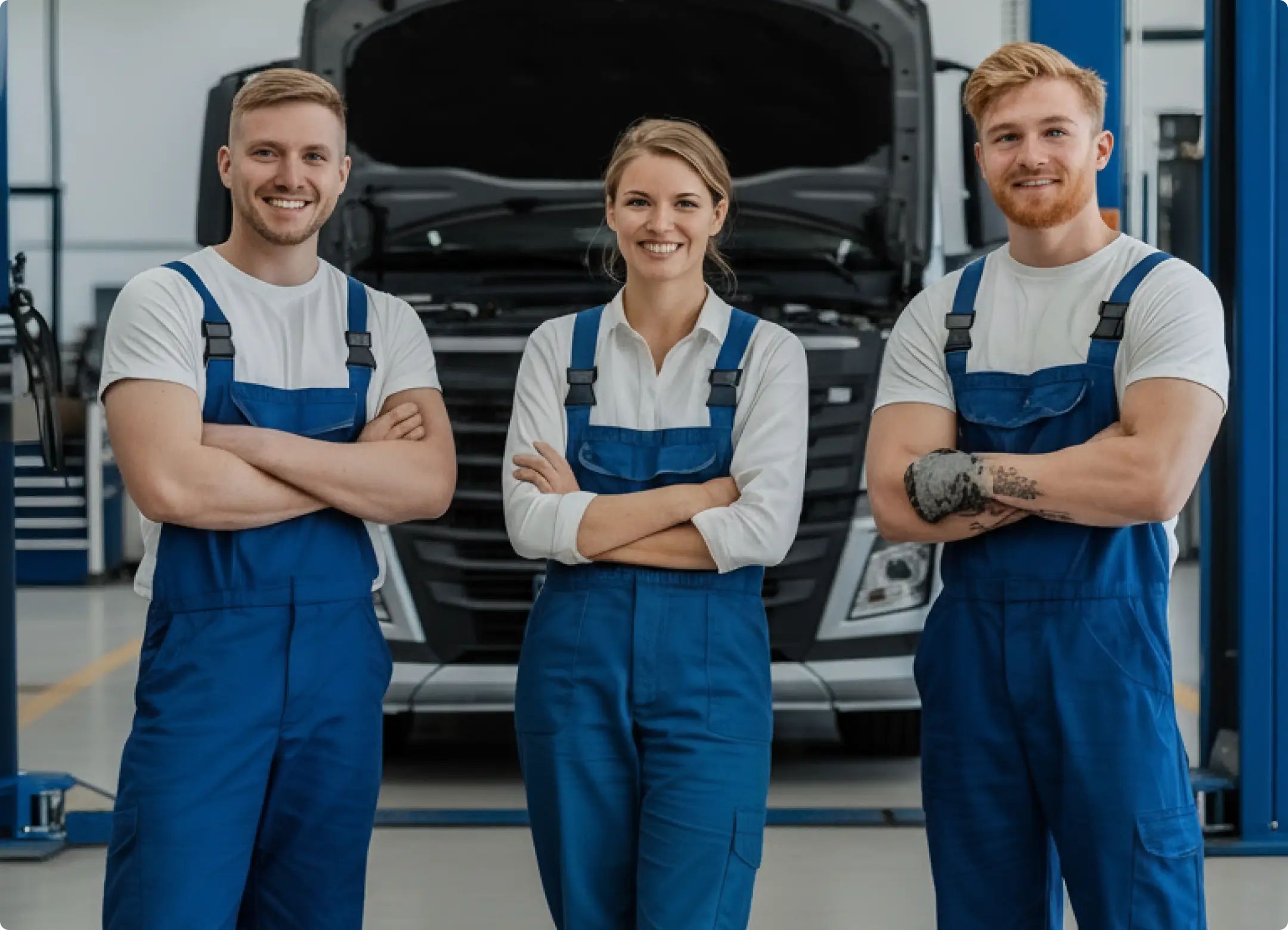 Three mechanics in blue overalls smiling.
